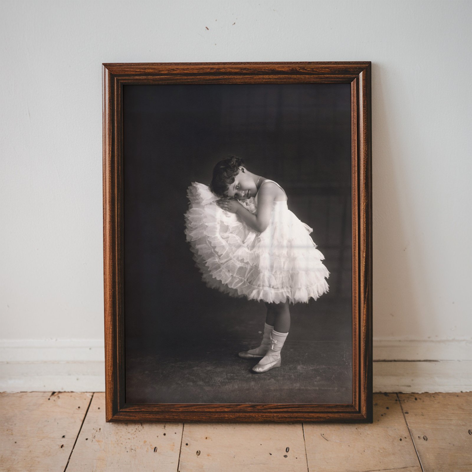 Vintage black and white portrait of a young ballerina in a layered white tutu posing gracefully against a dramatic dark background.